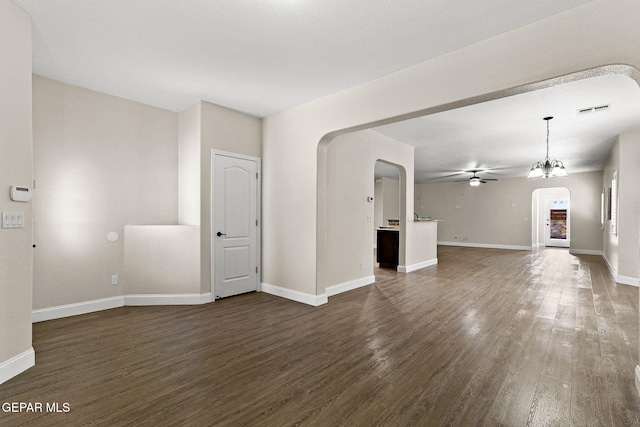 unfurnished living room with ceiling fan, visible vents, arched walkways, dark wood finished floors, and baseboards