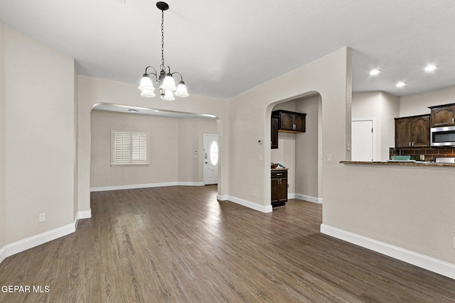unfurnished living room featuring arched walkways, baseboards, dark wood-style floors, a chandelier, and recessed lighting