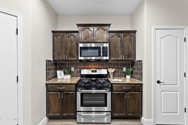 kitchen featuring light stone counters, a textured wall, appliances with stainless steel finishes, and backsplash