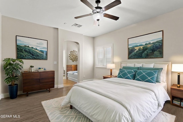bedroom with baseboards, arched walkways, wood finished floors, and visible vents