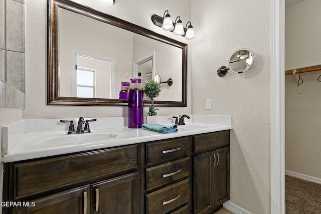 full bath featuring a sink, a textured wall, double vanity, and a spacious closet