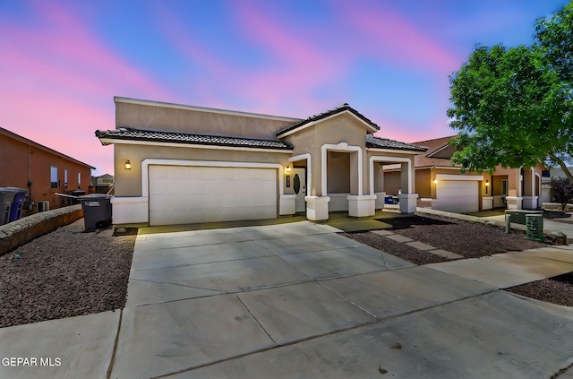 view of front of property featuring concrete driveway, an attached garage, a tile roof, and stucco siding