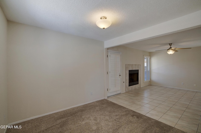 unfurnished living room with ceiling fan, light carpet, a tiled fireplace, baseboards, and light tile patterned floors