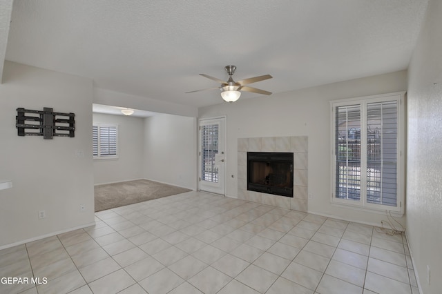 unfurnished living room with ceiling fan, light carpet, a fireplace, baseboards, and light tile patterned floors