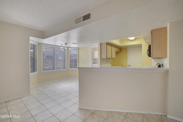 kitchen featuring a textured ceiling, a peninsula, baseboards, light tile patterned floors, and visible vents