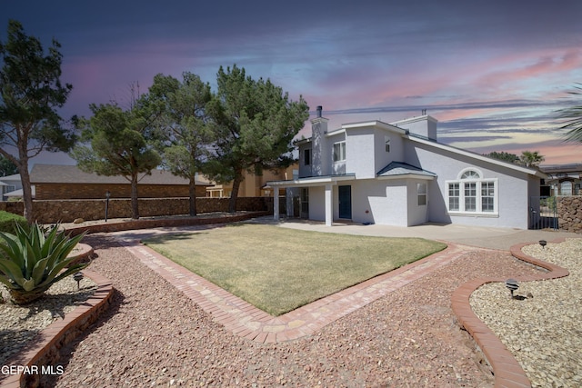 back of property at dusk featuring a yard, a patio, fence, and stucco siding