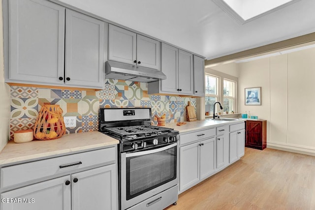 2723 Grant Ave, El Paso, TX 79930 - kitchen featuring gas range, under cabinet range hood, a sink, light wood finished floors, and decorative backsplash