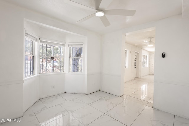 empty room with plenty of natural light, marble finish floor, and ceiling fan