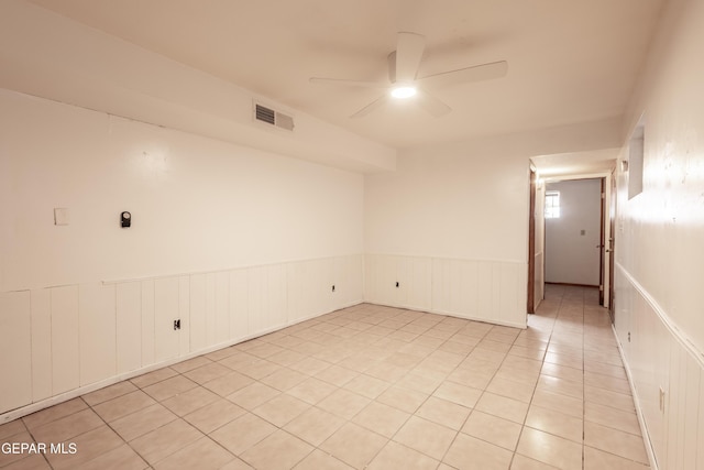 unfurnished room with visible vents, ceiling fan, a wainscoted wall, and light tile patterned floors