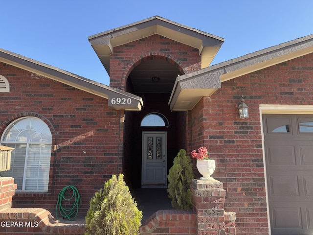 view of exterior entry with an attached garage and brick siding