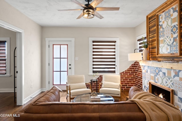living room with wood finished floors, baseboards, a lit fireplace, a ceiling fan, and a wealth of natural light