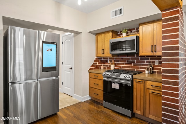 kitchen featuring appliances with stainless steel finishes, dark wood finished floors, baseboards, tasteful backsplash, and visible vents