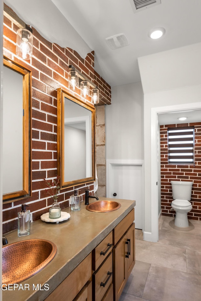 bathroom with double vanity, brick wall, visible vents, and a sink
