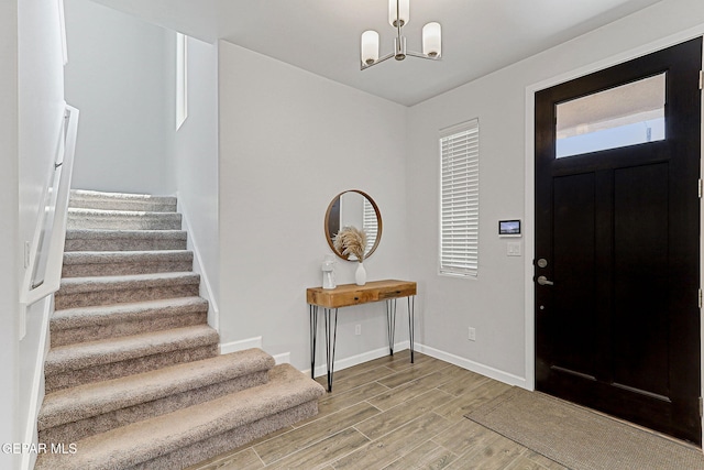 foyer entrance with stairway, baseboards, wood finished floors, and a notable chandelier