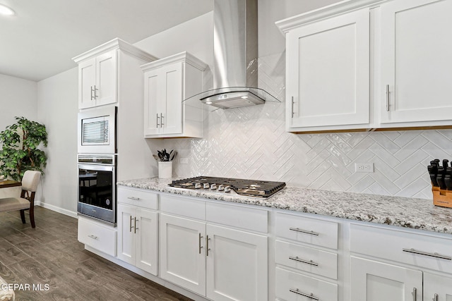 kitchen with wall chimney exhaust hood, appliances with stainless steel finishes, backsplash, and white cabinets