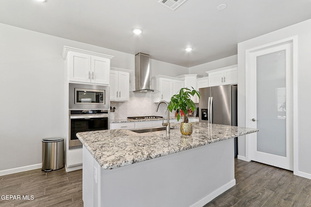 kitchen featuring dark wood-style flooring, visible vents, appliances with stainless steel finishes, a sink, and wall chimney exhaust hood