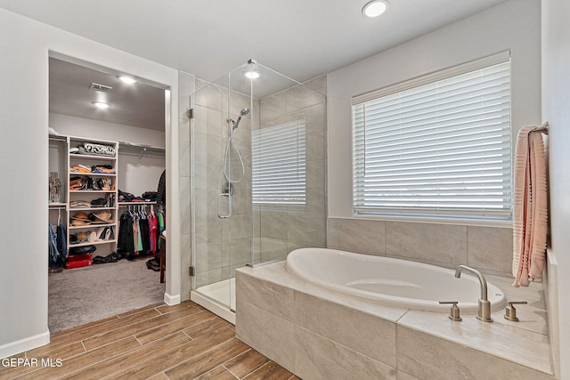 bathroom featuring wood finished floors, a spacious closet, visible vents, a garden tub, and a stall shower