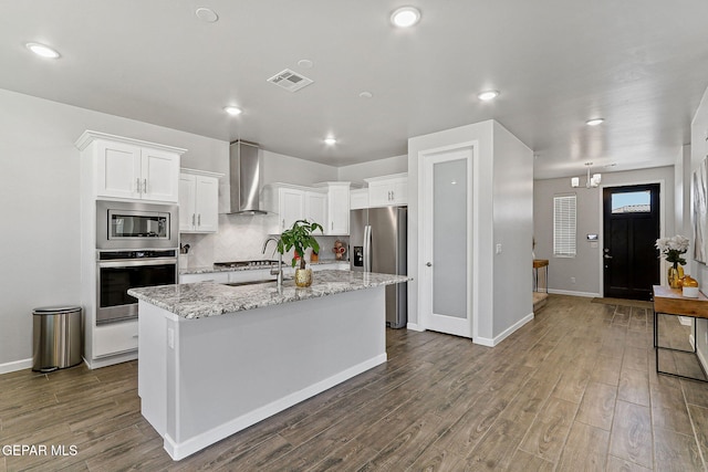 kitchen with wall chimney range hood, dark wood-style flooring, visible vents, appliances with stainless steel finishes, and white cabinetry