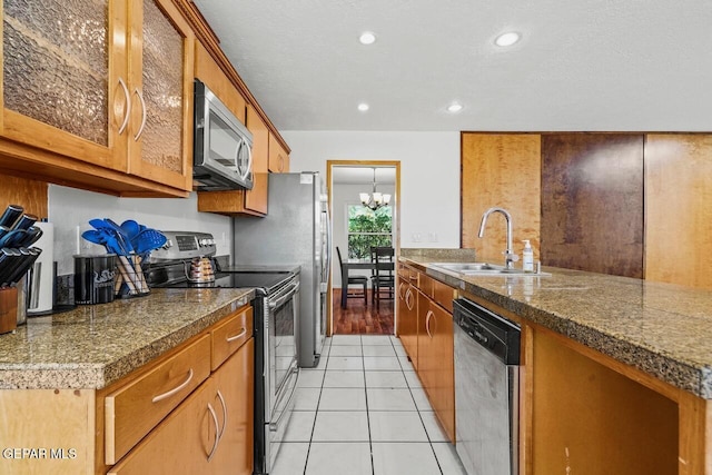kitchen featuring appliances with stainless steel finishes, a sink, tile countertops, a chandelier, and brown cabinetry