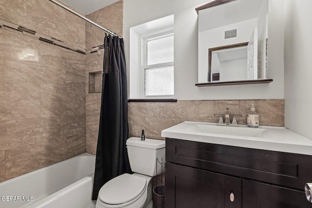 bathroom featuring tile walls, toilet, vanity, shower / bath combo, and wainscoting