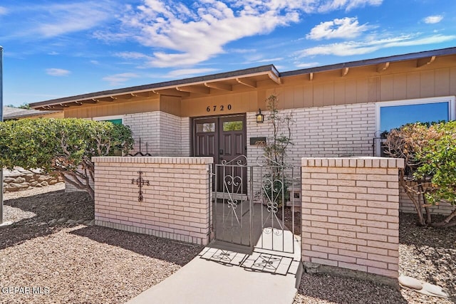 entrance to property with brick siding, a gate, and fence