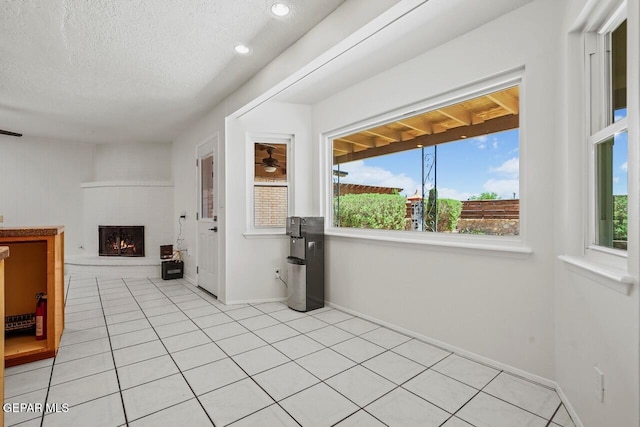 unfurnished living room featuring healthy amount of natural light, a fireplace, a textured ceiling, light tile patterned floors, and baseboards