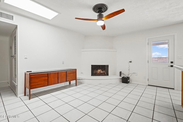 unfurnished living room featuring a ceiling fan, a lit fireplace, light tile patterned floors, and baseboards