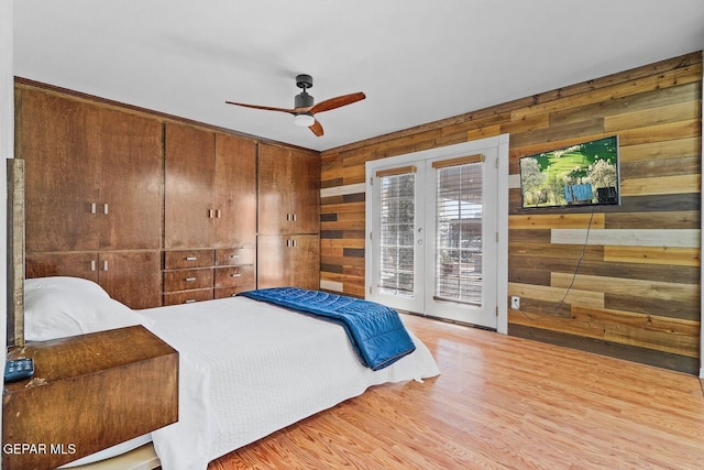 bedroom with wooden walls, access to exterior, light wood-type flooring, ceiling fan, and french doors