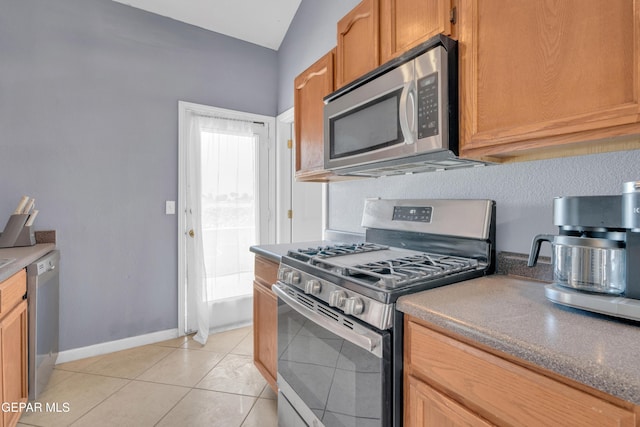 kitchen with baseboards, lofted ceiling, light tile patterned flooring, and stainless steel appliances