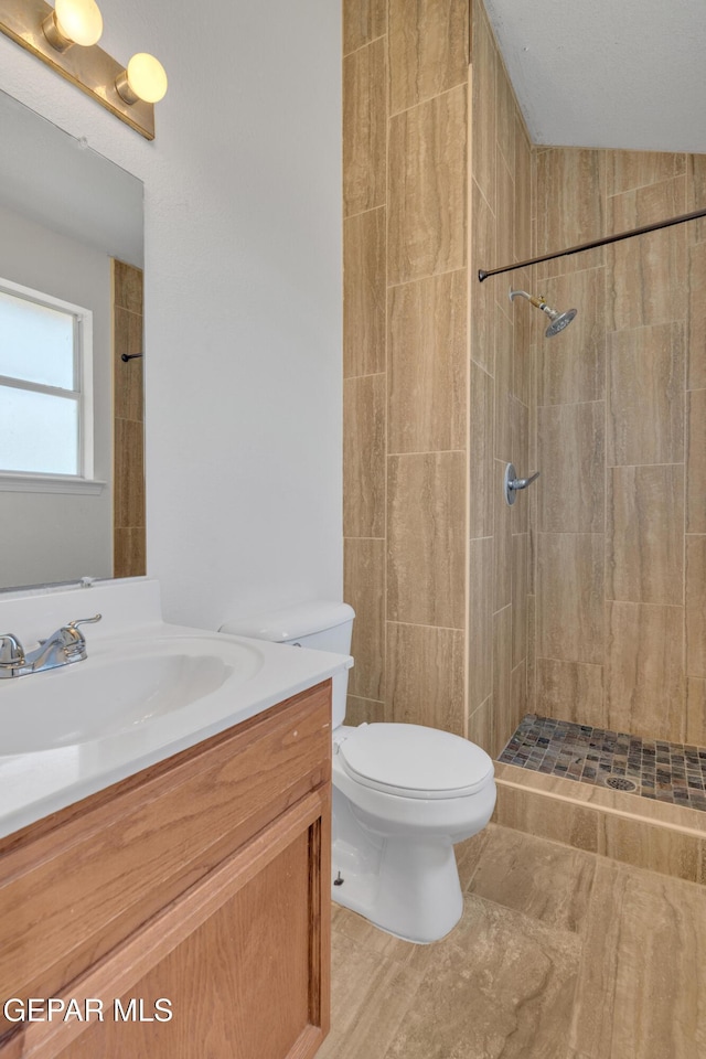 full bathroom with vanity, a tile shower, and toilet