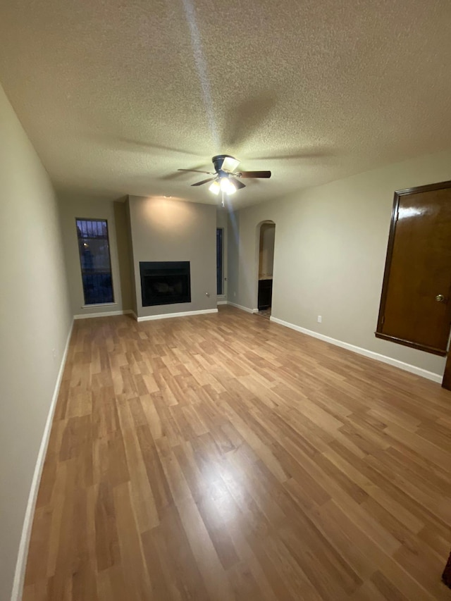 unfurnished living room with arched walkways, ceiling fan, baseboards, and light wood finished floors