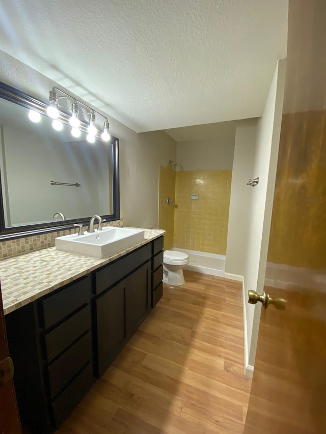 bathroom featuring a textured ceiling, a shower, wood finished floors, vanity, and toilet
