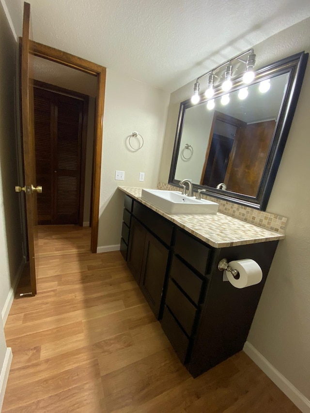 bathroom featuring a textured ceiling, baseboards, vanity, and wood finished floors