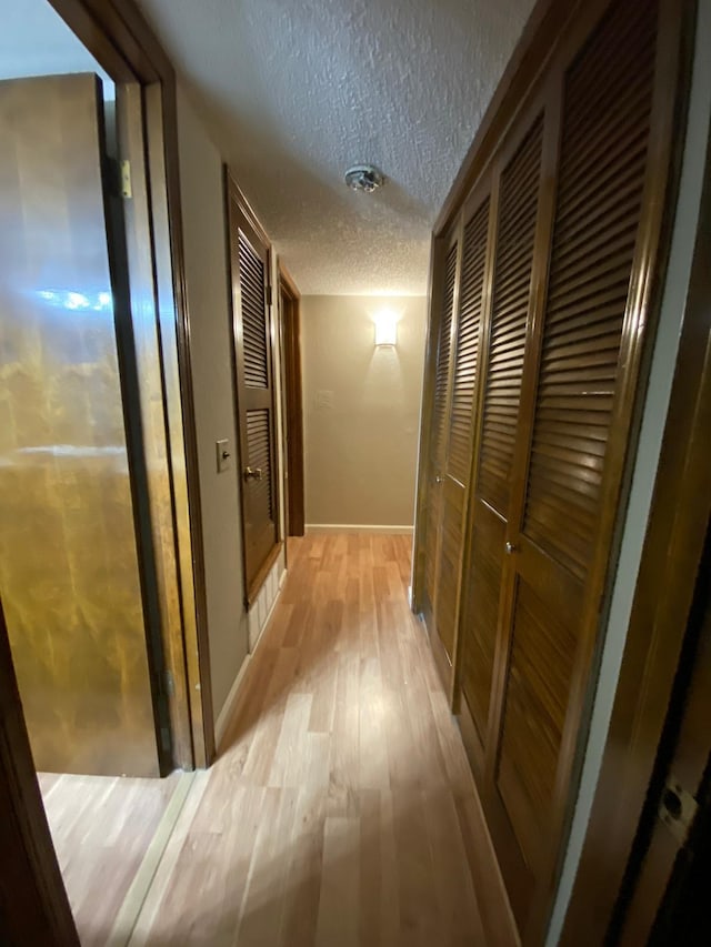hall with a textured ceiling, baseboards, and light wood-type flooring
