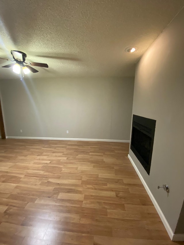 unfurnished living room with ceiling fan, a fireplace, a textured ceiling, baseboards, and light wood-type flooring