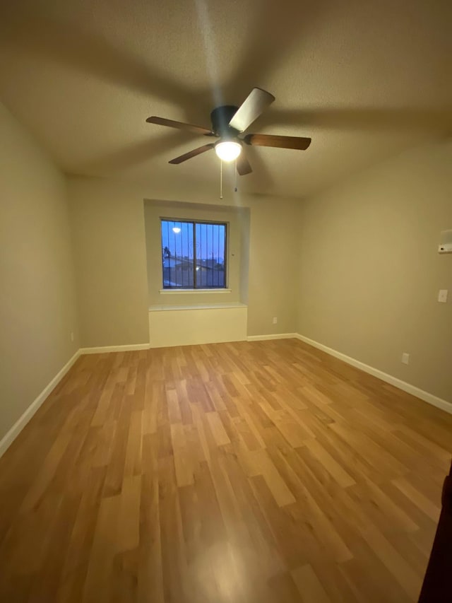 spare room featuring baseboards, ceiling fan, and light wood finished floors