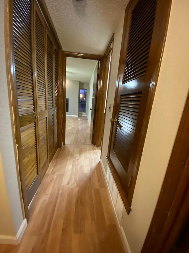 corridor with light wood-style floors, baseboards, and a textured ceiling