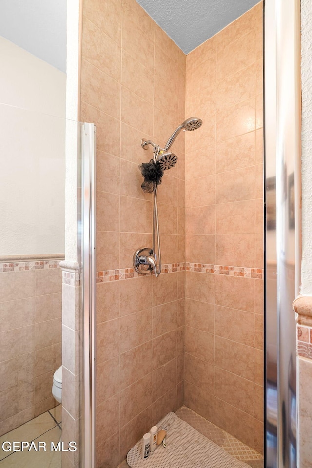 1829 Paseo Real Cir, El Paso, TX 79936 - bathroom featuring toilet, tile patterned floors, a wainscoted wall, tile walls, and a stall shower