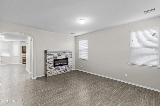 unfurnished living room featuring visible vents, arched walkways, baseboards, and a tile fireplace