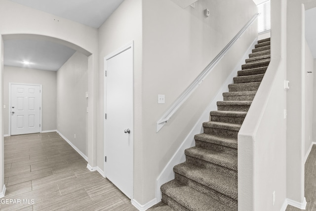 stairway with arched walkways, baseboards, and wood finished floors