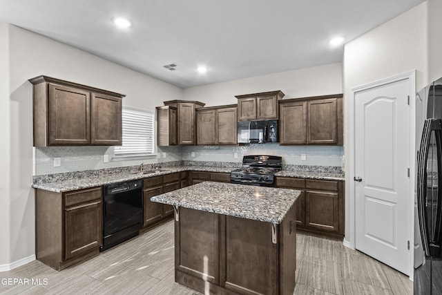 kitchen featuring light stone countertops, dark brown cabinetry, tasteful backsplash, visible vents, and black appliances