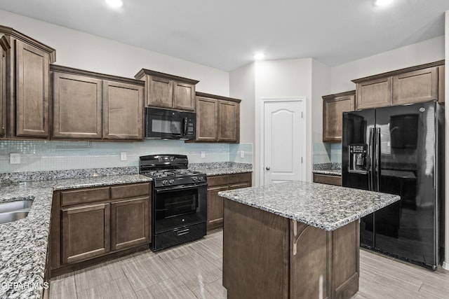 kitchen featuring decorative backsplash, dark brown cabinetry, a center island, light stone countertops, and black appliances