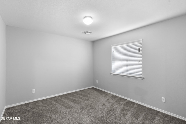 spare room featuring dark colored carpet, baseboards, and visible vents
