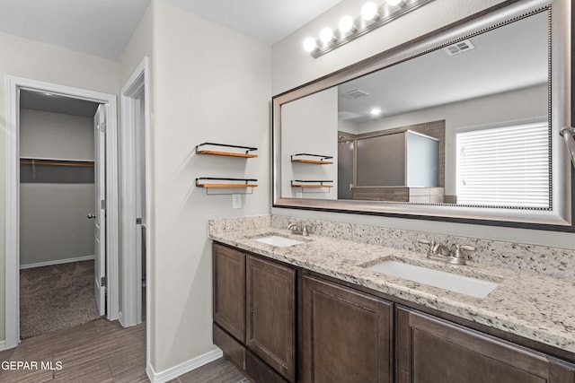 bathroom with a walk in closet, visible vents, a sink, and wood finished floors