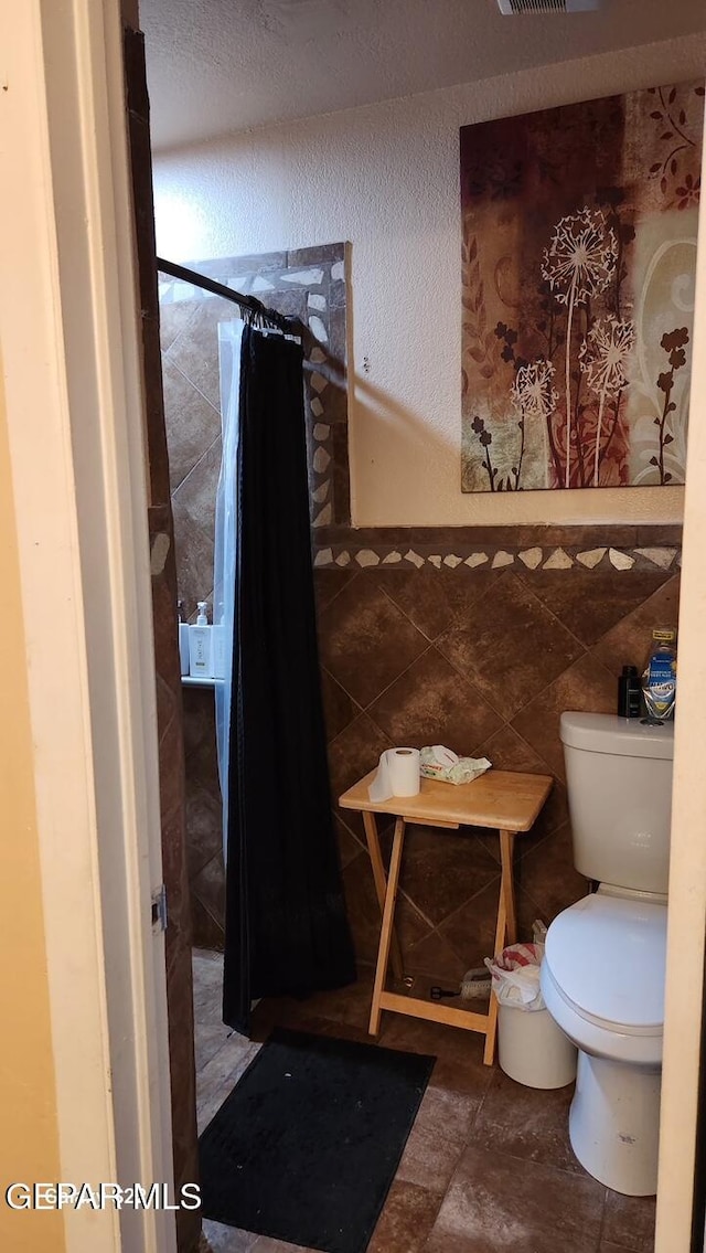 11325 Tom Ulozas Dr, El Paso, TX 79936 - bathroom featuring toilet, a shower with curtain, tile walls, and a textured wall