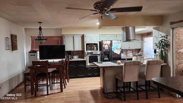 11325 Tom Ulozas Dr, El Paso, TX 79936 - kitchen with stainless steel appliances, wall chimney exhaust hood, a peninsula, light wood-style floors, and a kitchen breakfast bar