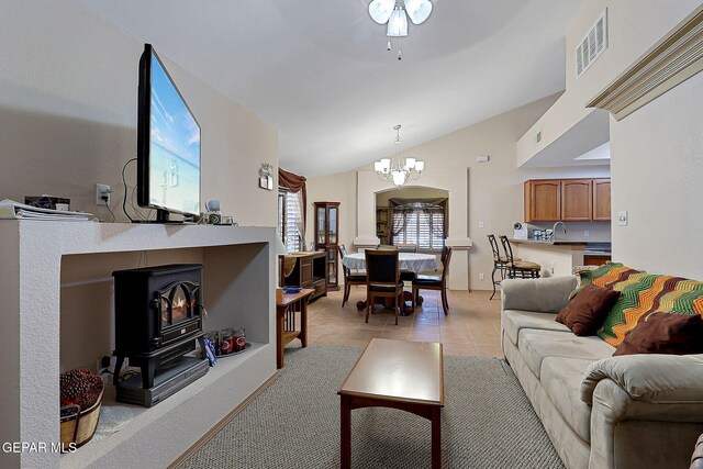 living area featuring visible vents, a wood stove, ceiling fan with notable chandelier, lofted ceiling, and light tile patterned flooring
