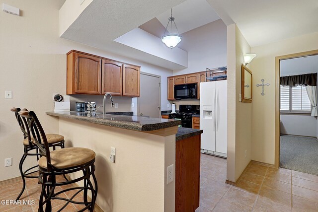 kitchen with a kitchen breakfast bar, brown cabinetry, a sink, black appliances, and a peninsula