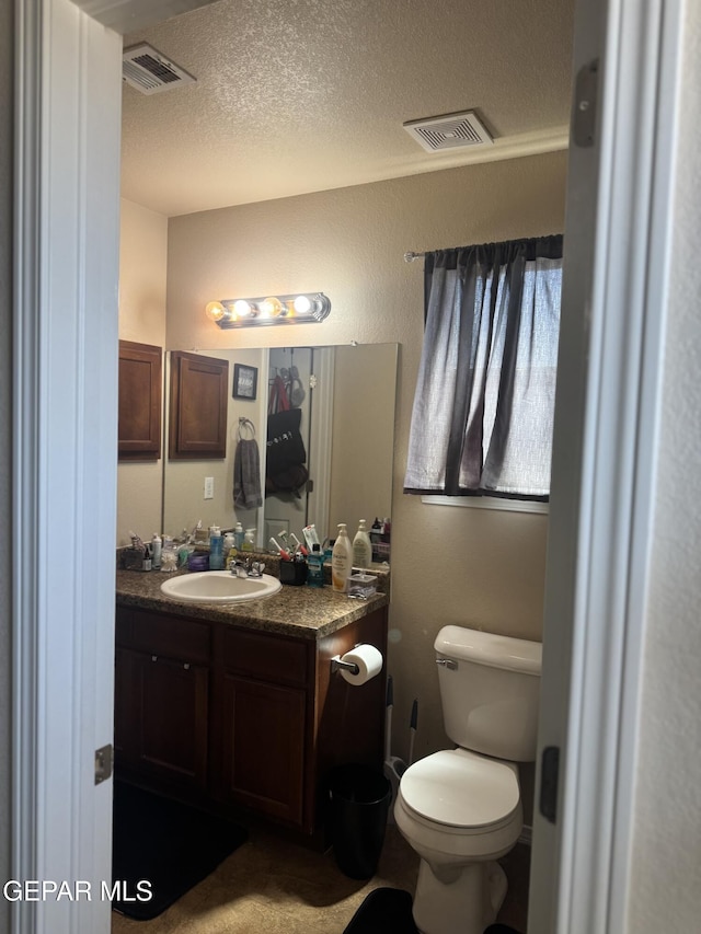 half bathroom with toilet, a textured ceiling, visible vents, and vanity