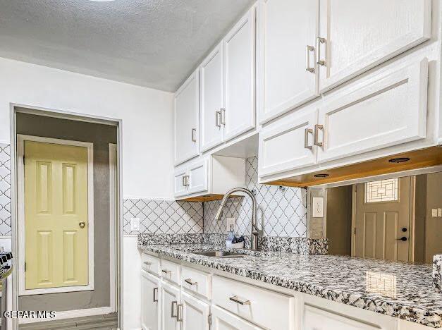 kitchen featuring white cabinetry, light stone countertops, and a sink